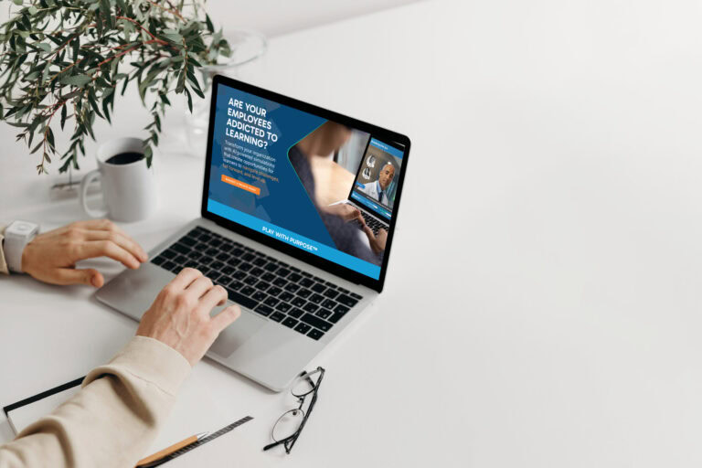 Person using a laptop with a website about employee addiction to learning on the screen, on a white desk with a plant, glasses, and a pen.